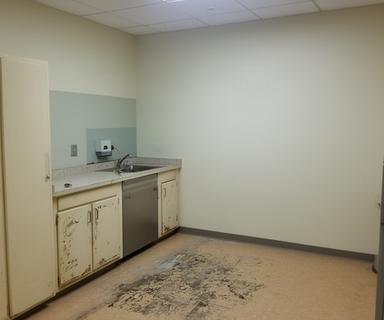 Clinic treatment room with older cabinetry, worn flooring, and existing service locations before an improvement plan